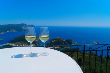 Arka planda Korfu deniz manzaralı iki kadeh beyaz şarap.