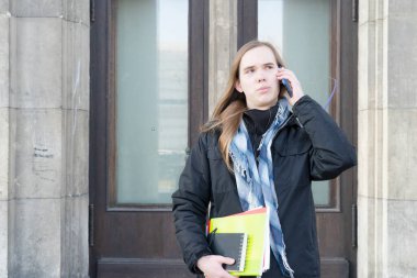 Erkek öğrenci üniversite girişinin önünde telefonla konuşuyor.