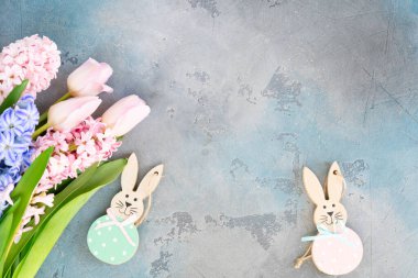 Easter scene with fresh tulips and hyacinth flowers and Easter bunnies over gray background, copy space