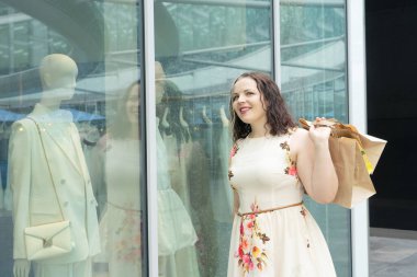 Ekolojik el sanatları alışveriş torbalarıyla dükkan vitrinine bakıp alışverişin tadını çıkaran mutlu kavisli kadın. Tüketim, alışveriş, yaşam tarzı konsepti