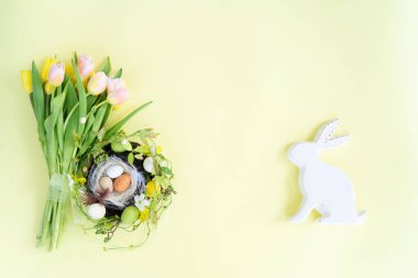 Easter scene with colored eggs in nest, bunny and handmade bunny, top view with copy space