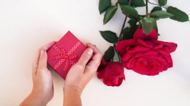 Gift for Valentines Day - someone hands placing gift box near red roses, top view