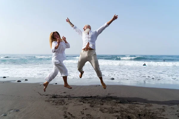 lifestyle with caucasian senior couple jump fun on beach, happy in love romantic and relax time, tourism of elderly family pleople, leisure and activity travel after retirement in vacations and summer