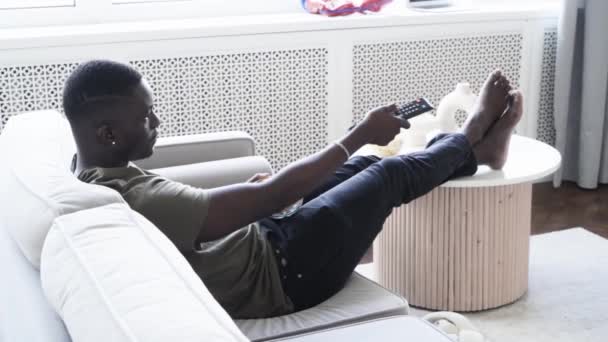 Young Afroamerican Man Watching Sofa Eating Chips — Stock Video