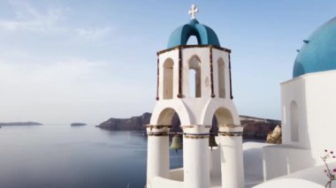 Establishing shot of Oia, white church belfry, blue domes and volcano caldera with sea landscape, establishing shot of Santorini island, Greece