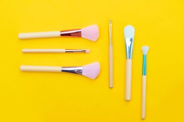 Asgari modern kozmetik sahnesi, sarı arkaplan üzerine kurulmuş makyaj fırçaları.