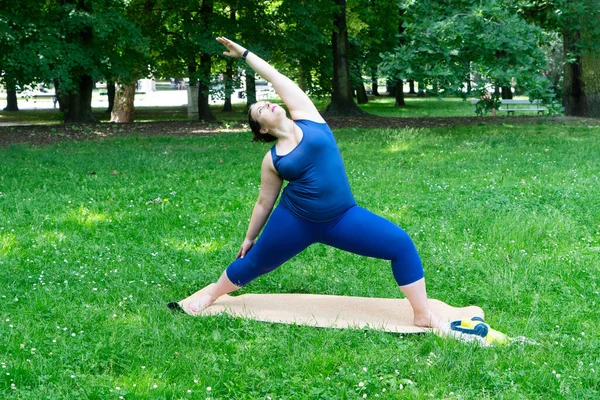 Woman and sports, exercise for weight loss in the fresh air. Happy curvy 40s woman doing workout stretch routine outdoor at green city park