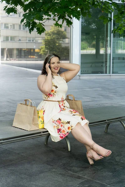 Happy curvy woman with ecological shopping bags sitting and talking on mobile phone enjoying in shopping. Consumerism, shopping, lifestyle concept