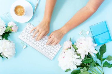 Düz ev üstten görünüm office çalışma alanı someones el yazma ile beyaz çerçeve modern klavye, notebook ve Şakayık çiçekleri mavi arka plan üzerinde yatıyordu