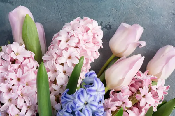Paskalya sahnesinde taze laleler ve sümbül çiçekleri gri arka planda.