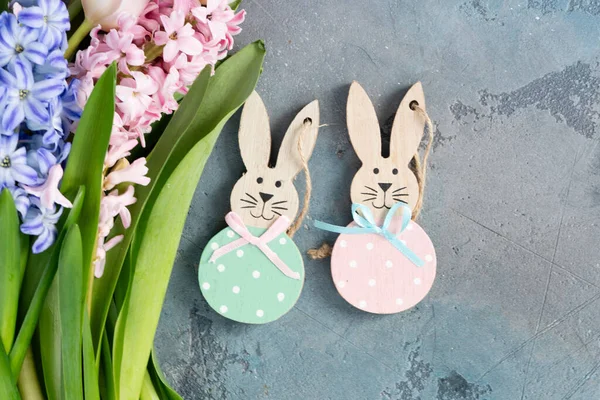 Paskalya sahnesi. Taze laleler, sümbül çiçekleri ve gri arka planda iki Paskalya tavşanı.
