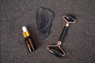 Gua sha, yüz masajı silindiri siyah kum arka planında doğal taştan yapılmış.