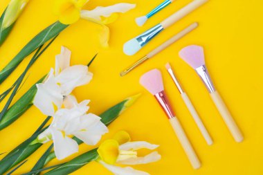 Makyaj fırçaları ve sarı arkaplan üzerine kurulmuş çiçeklerle en az modern kozmetik sahne