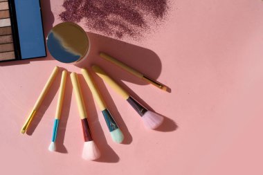 Makyaj fırçaları ile minimum modern kozmetik sahnesi pembe arkaplan üzerine parıltı ve gölge örtüsüyle kurulmuş, boşluğu kopyala