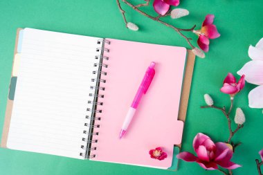 Yeşil zemin üzerinde çiçekler olan pembe manolya ağacı dalı, kopyalama alanı için defter sayfası aç