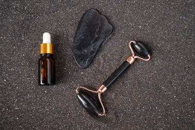 Gua sha, yüz masajı silindiri siyah kum arka planında doğal taştan yapılmış.