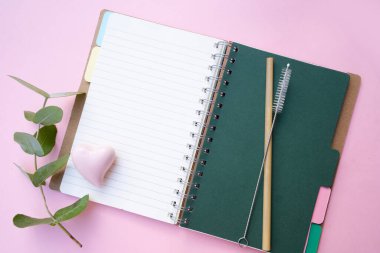 Açık defter ve yeşil okaliptüs yapraklı sıfır atık kavramı pembe arkaplan üzerinde