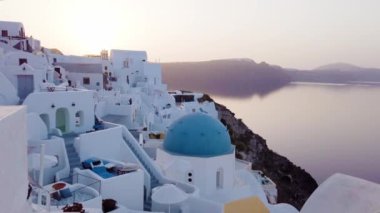 Beyaz kilise çan kubbesi, mavi kubbeler ve deniz manzaralı volkan kalderası, Yunanistan 'ın Santorini adasının çekimini oluşturuyor.