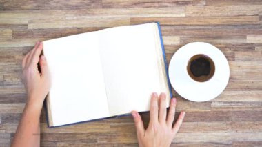 Hands open book on empty page, top view of the desk wuth coffee