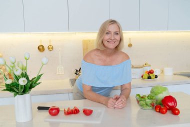 Neşeli, son sınıf öğrencisi bir kadın şık mutfağında taze malzemelerle lezzetli yemekler hazırlar ve sağlıklı bir yaşam sürmesini sağlar.