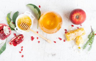 rosh hashana holiday - honey jar with red apple and pomergranate over white desk background. border with copy space