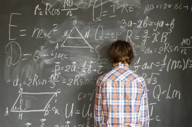 Genç çocuk, siyah tahtada karmaşık matematik formülleriyle sorun yaşıyor.