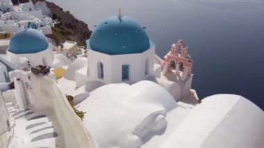 Establishing shot of Oia, white church belfry, blue domes and volcano caldera with sea landscape, establishing shot of Santorini island, Greece