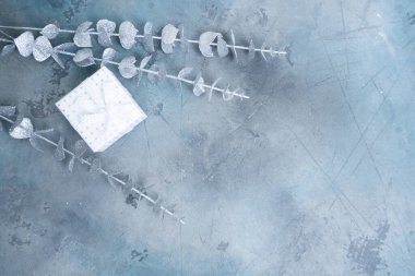 Beyaz bir hediye kutusu, süsler ve dokulu mavi bir yüzeyde yeşillik içeren şık bir tatil düzenlemesi..