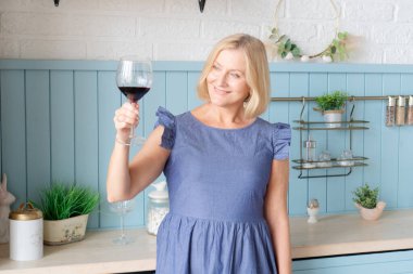 Sofistike bir kadın, neşe ve zarafet saçıyor şık bir mutfakta nefis bir kadeh kırmızı şaraptan zevk alıyor.