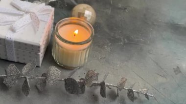Sakin bir tatil düzeninde bir mum, zarif bir sabun ve desenli bir arka planda şık gümüş yapraklar bulunur.