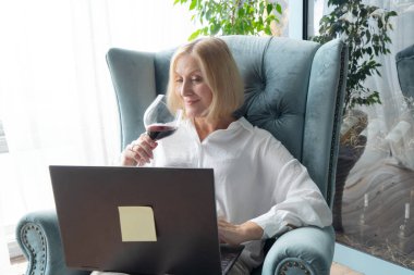 Sofistike bir kadın, neşe ve zarafet saçıyor, bilgisayarını kontrol ederken bir bardak nefis kırmızı şaraptan zevk alıyor.