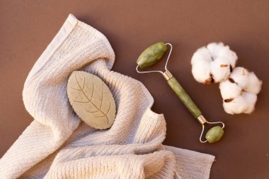 Gua sha, doğal taştan yapılmış yüz masajı silindiri, pamuk tomurcukları, spa konsepti, 2025 yılının mocha mus rengi.