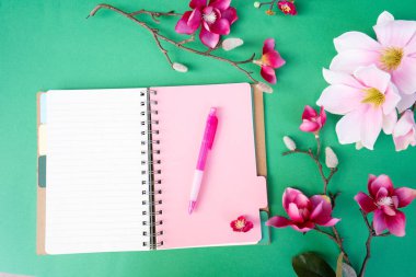 Yeşil zemin üzerinde çiçekler olan pembe manolya ağacı dalı, kopyalama alanı için defter sayfası aç