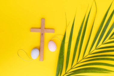 A wooden cross with eggs and lilies on a palm leaves pattern, a Palm Sunday theme.