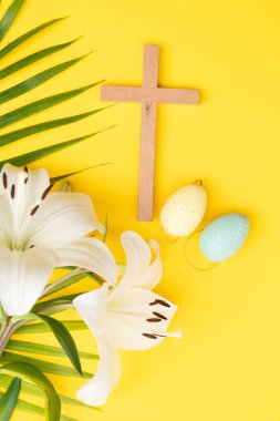 A wooden cross with eggs and lilies on a palm leaves pattern, a Palm Sunday theme.