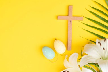 A wooden cross with eggs and lilies on a palm leaves pattern, a Palm Sunday theme.