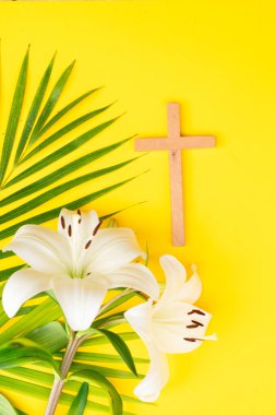 A wooden cross with eggs and lilies on a palm leaves pattern, a Palm Sunday theme.