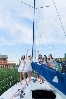 Güneşli bir günde, şık beyaz kıyafetler giymiş beş arkadaş bir yelkenlide kutlama yapmak için toplanır.