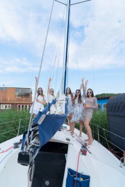 Güneşli bir günde, şık beyaz elbiseler giymiş arkadaşlar bir yelkenlide kutlama yapmak için toplanırlar.