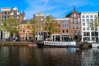 Hollanda, Amsterdam 'da kanal suyu üzerinde eski tarihi evler ve ağaçların cepheleri