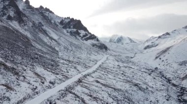 Aerial drone landscape reveal shot of snow summit with ice glacier and and rocky hills at mountain valley in Almaty Kazakhstan