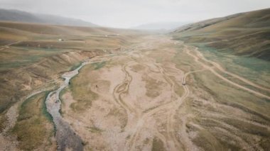 Kazakistan 'daki Assy Platosu' nda Orta Asya nehri yakınlarındaki dağlarda çakıllı yol boyunca giden off-road aracının üzerindeki hava aracı.