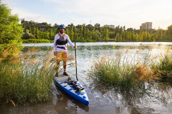 Ayağa kalkmış kürek çeken adam Kazakistan 'ın Almaty kentindeki Sairan dağlık gölünde SUP kullanıyor..