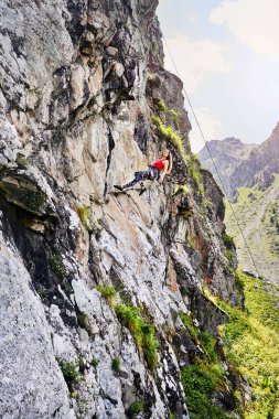 Kırmızı gömlekli, uzun saçlı güçlü bir kadının portresi Kazakistan 'daki Tyan Shan dağlarındaki yüksek dikey kayaya tırmanıyor.