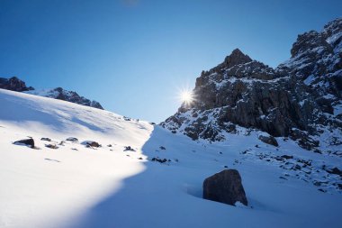 Yüksek karlı dağlarda güneşli bir gün, Kazakistan 'da kış zamanı mavi gökyüzüne vuran güneş ışığıyla parıldıyor. 