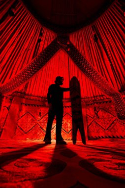 Yurt 'un iç kesimlerinde kırmızı ışıkla aydınlatılan etnik desenli halı karşısında kayak yapan insan silueti. Taşra sürücüsü spor konsepti.