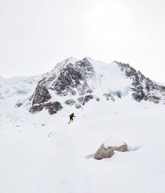 Sırt çantalı küçük adam güzel dağlarda kar tepesinde yürüyor Almaty, Kazakistan 'daki bulutlu gökyüzüne karşı. 
