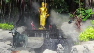 Bangkok 'taki Wat Saket Altın Dağ Tapınağı' nda şelaleli ve spreyli tropikal bahçede altın Buda heykeli.