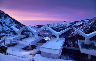 Landscape of glowing Medeu skating rink from cafe swallow old USSR architecture in Tian Shan mountains at pink sunset in Almaty city, Kazakhstan