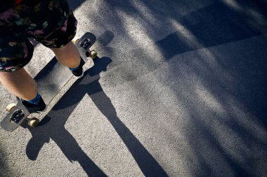 Man Skater at his longboard at mountain road close up shot at morning bright sunlight and harsh shadow